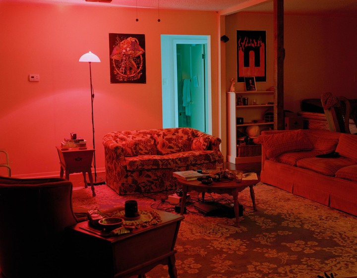 A living room is illuminated by red light, with a blue-lit doorway visible in the background.