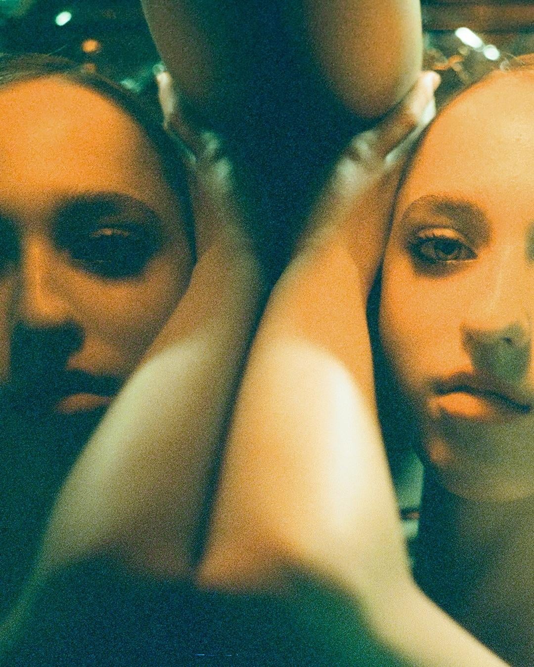 Two women are visible in a close-up portrait with their arms intertwined.