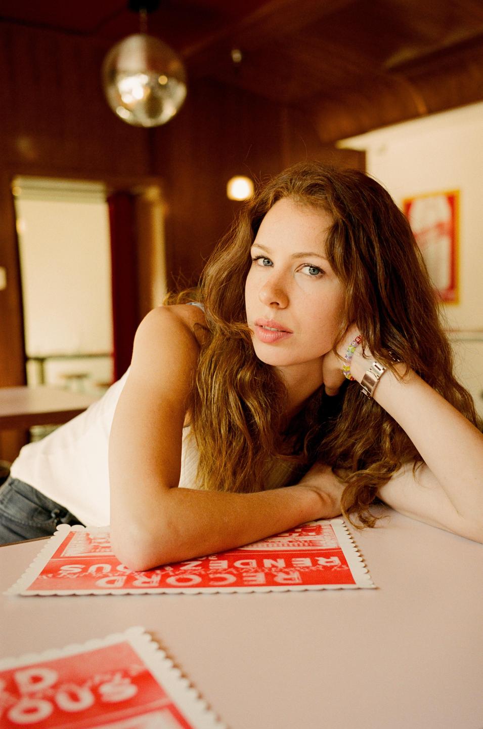 A woman with long, wavy hair rests her head on her arm at a table with a red placemat.