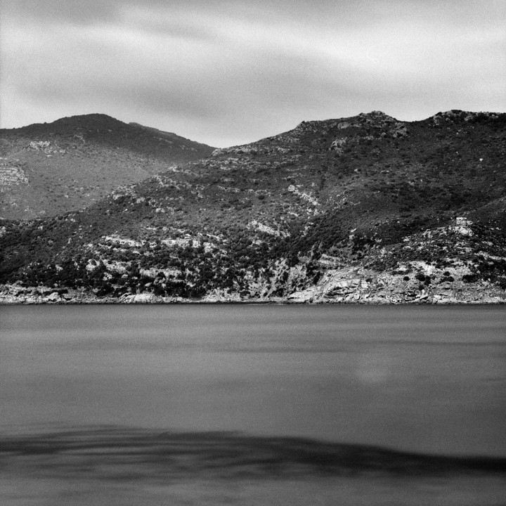 A body of water sits in front of a range of hills covered in sparse vegetation.