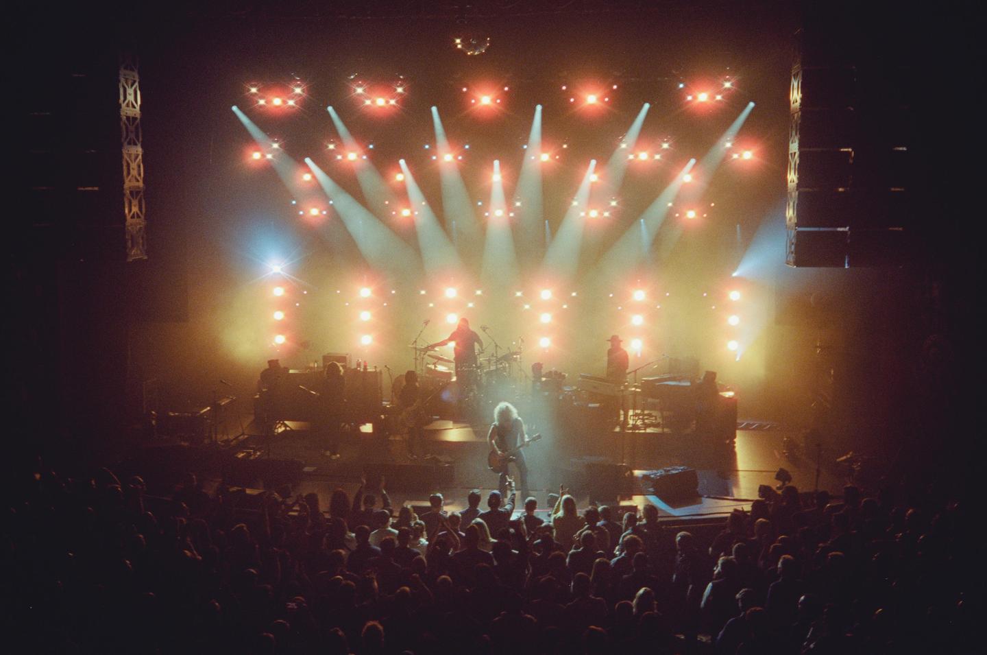 A band performs on stage under bright lights to a large audience.