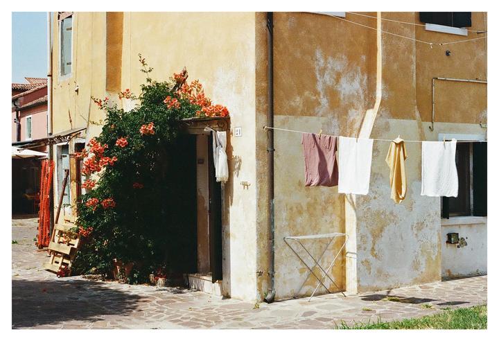 Laundry hangs on a clothesline in front of a building with an overgrown entrance.