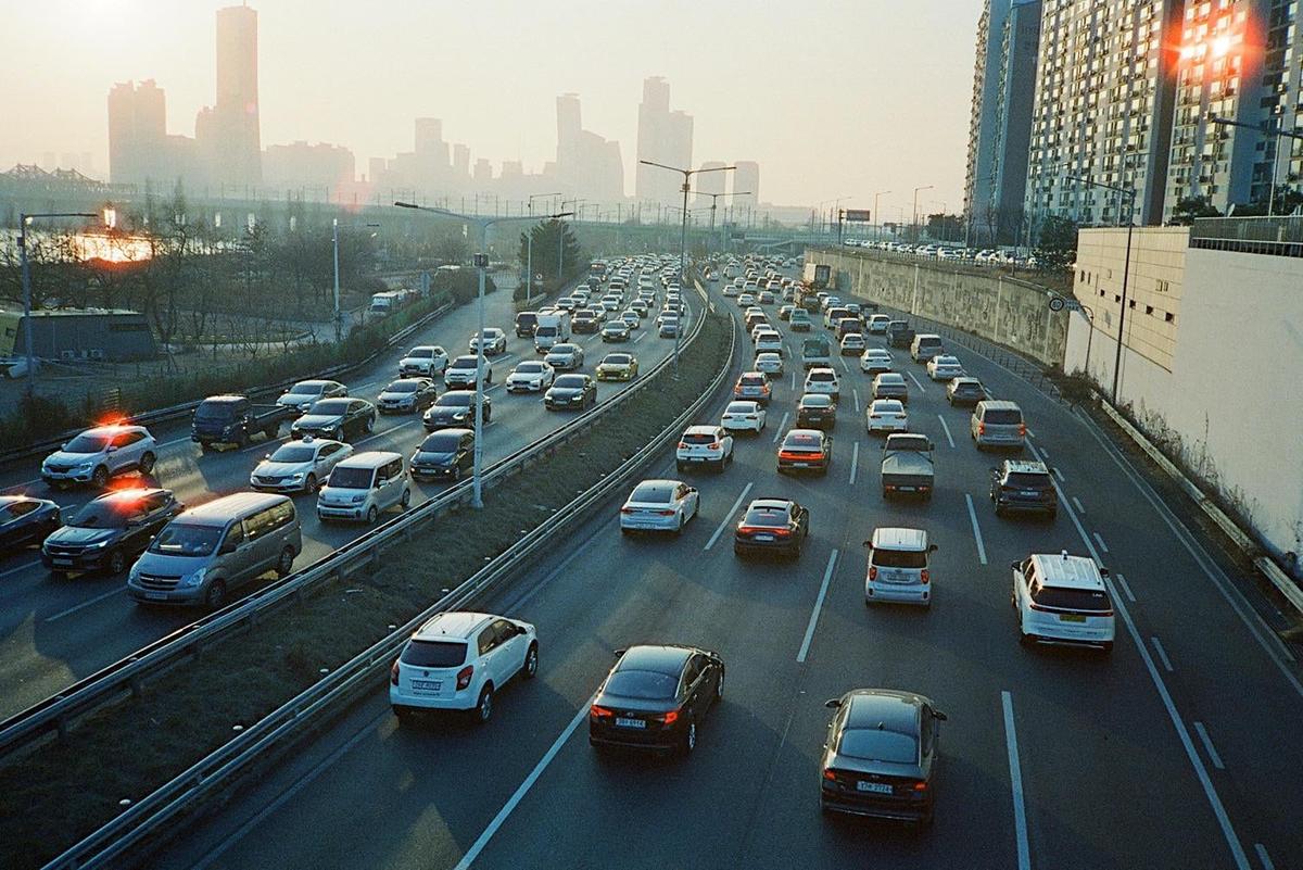 A multi-lane highway is filled with cars during golden hour, with a city skyline in the hazy distance.