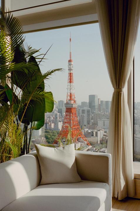 A view of the Tokyo Tower and city skyline from a window with a couch, curtain, and plant in the foreground.