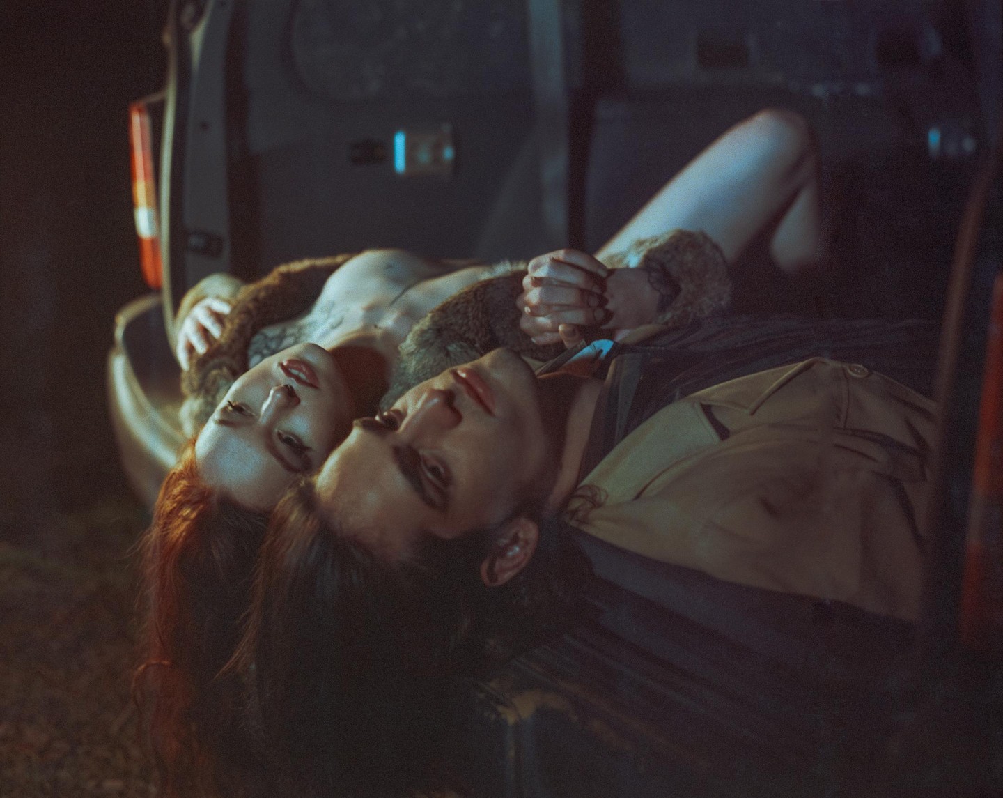 A couple is lying in the trunk of a car at night.