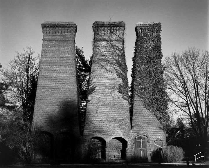 Three tall brick structures with arched openings at their bases stand among trees, with two of them partially covered in vines.