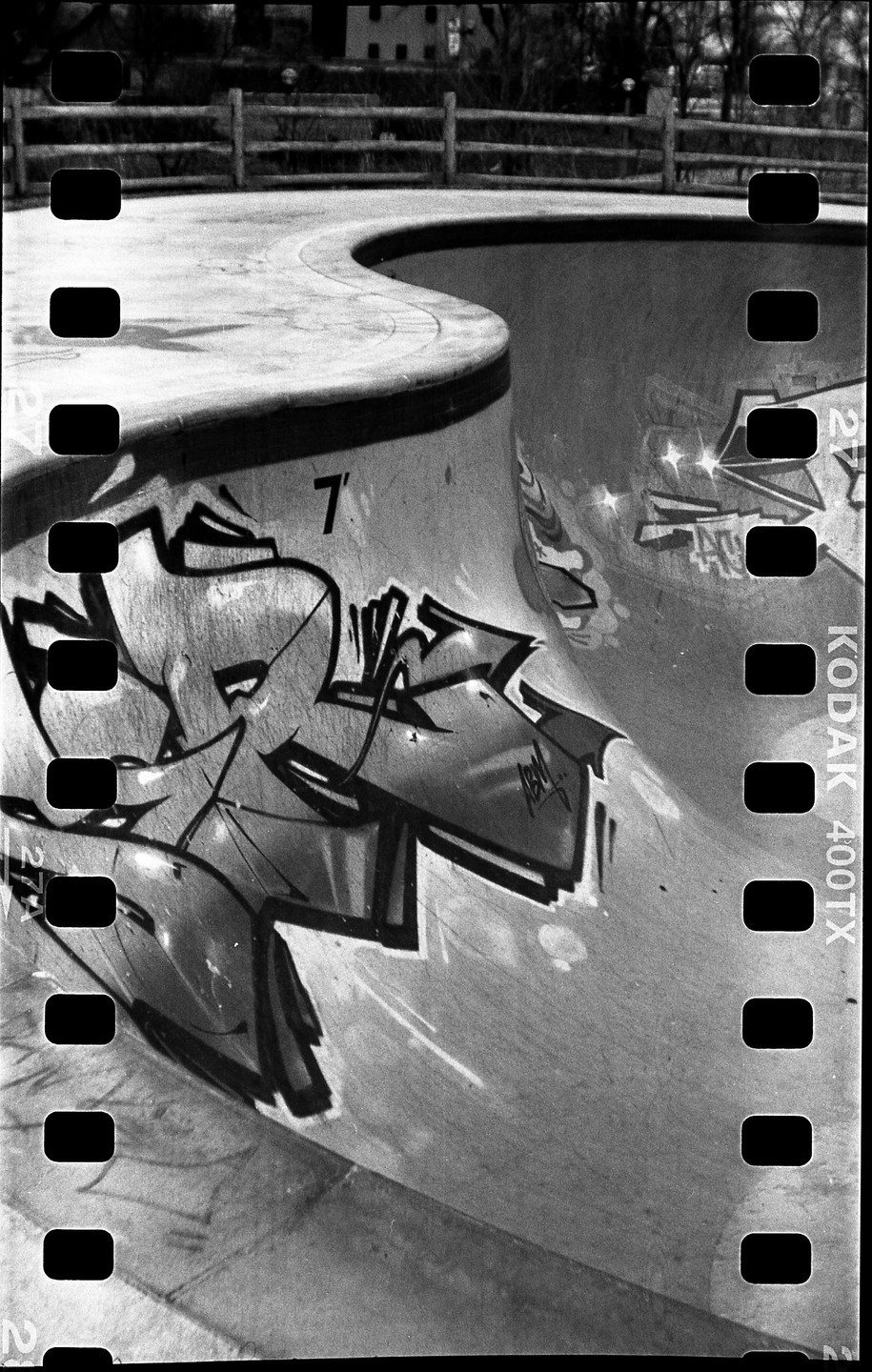 A skatepark bowl with graffiti is visible through a film strip.