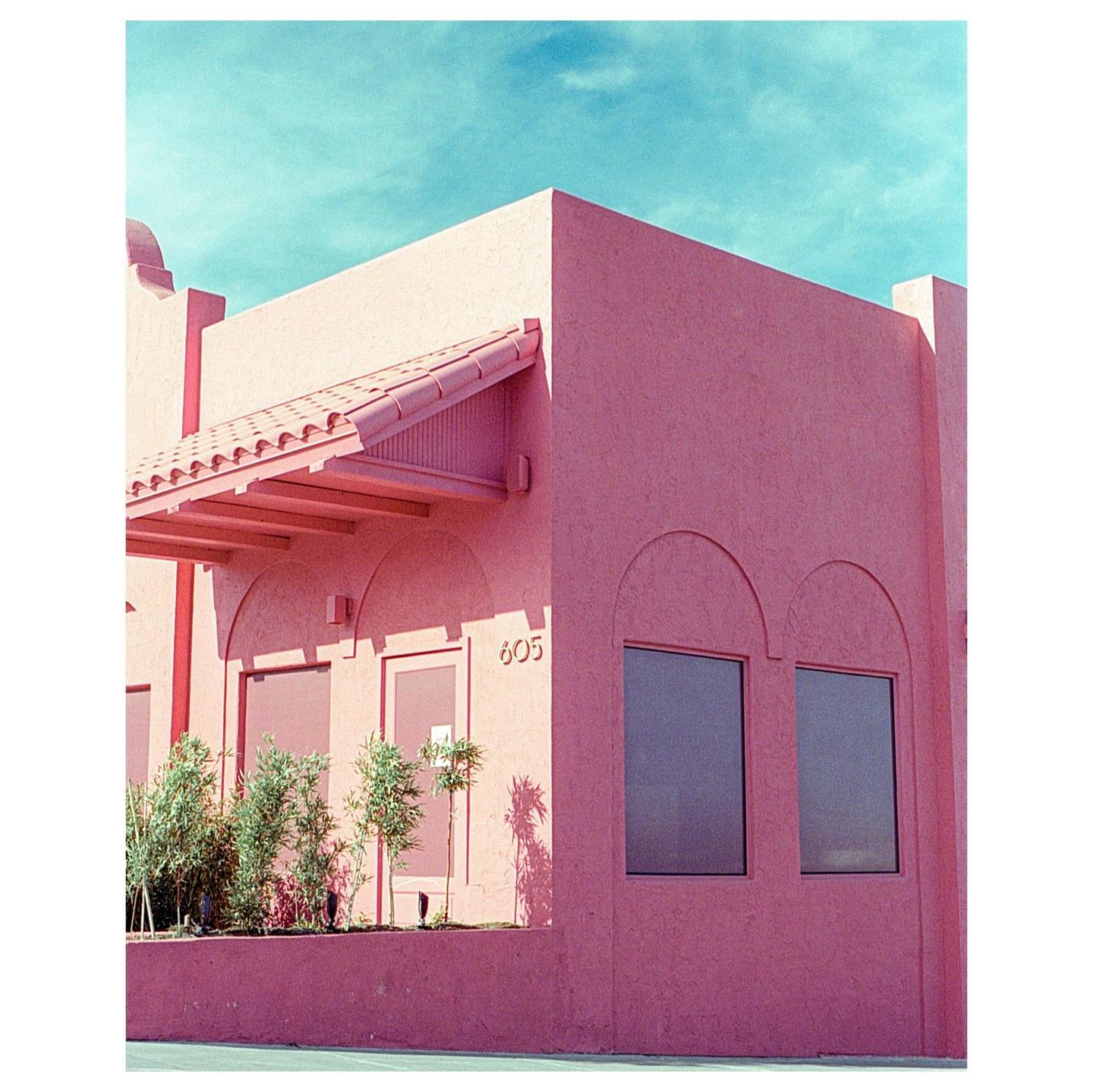 A pink building with an awning and two arched windows is shown under a bright blue sky.