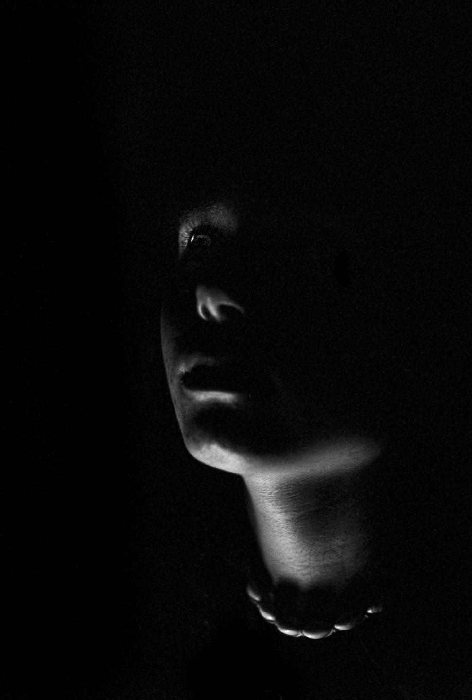 A woman's face is partially illuminated from below in a black and white portrait.
