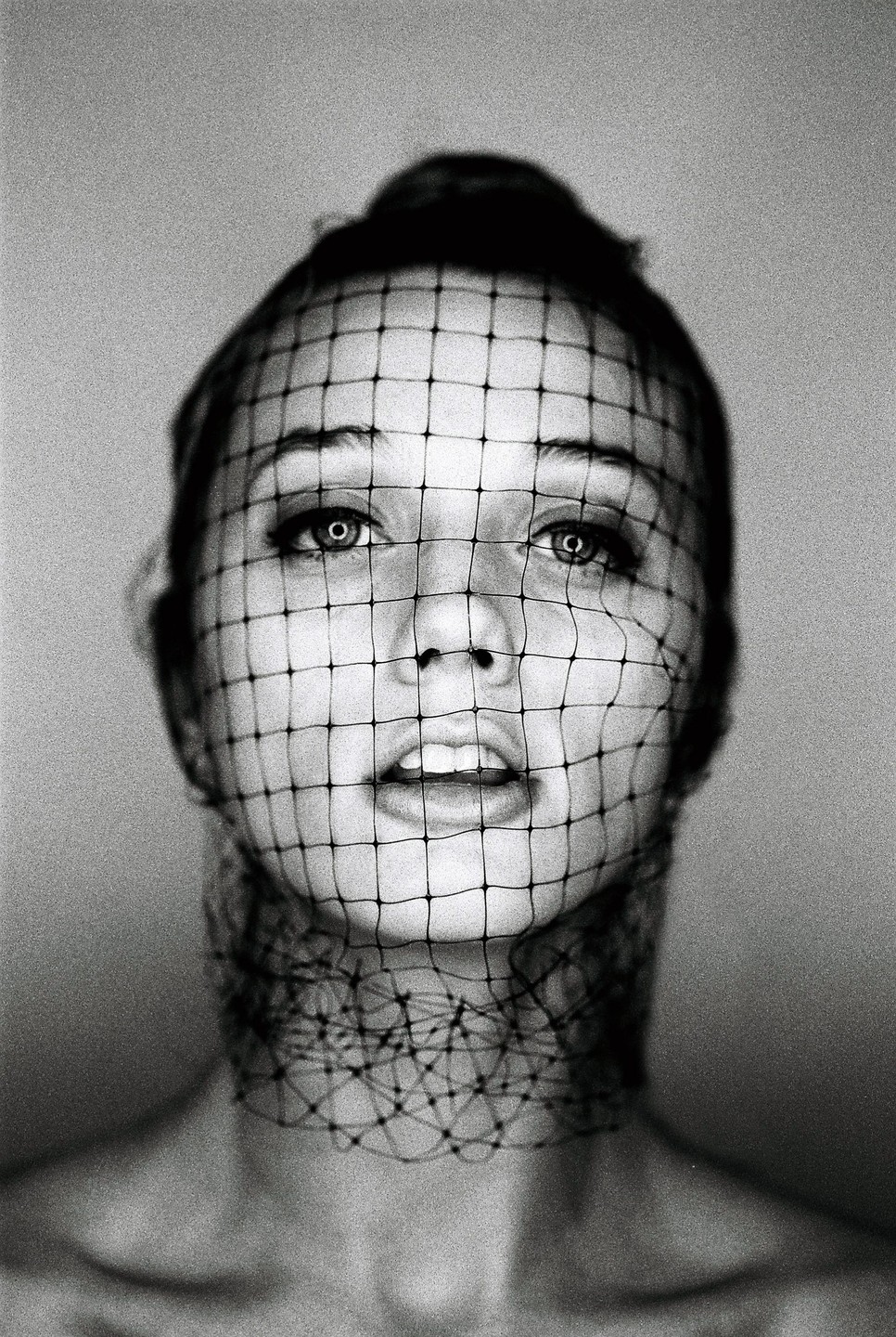 A woman with a net covering her face and neck looks directly at the viewer.