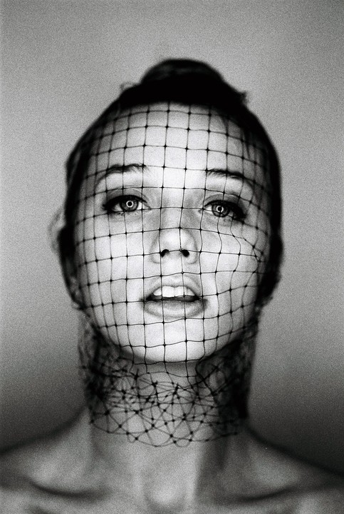A woman with a net covering her face and neck looks directly at the viewer.