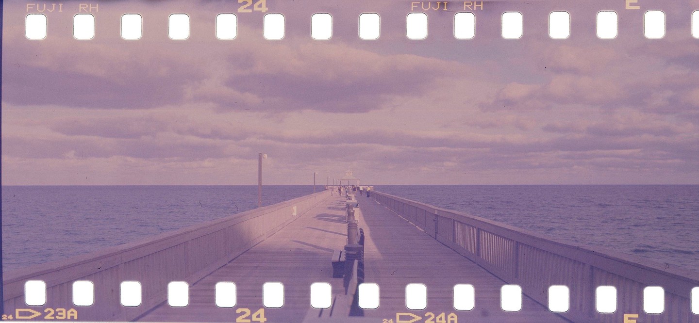 A long pier extends into the ocean under a cloudy sky, with people visible in the distance.