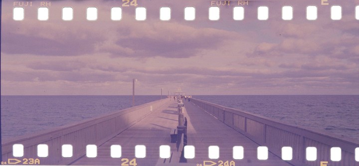 A long pier extends into the ocean under a cloudy sky, with people visible in the distance.