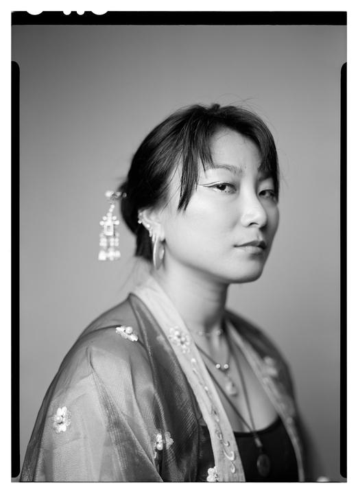 A woman with a decorative hairpiece and earrings looks towards the viewer.