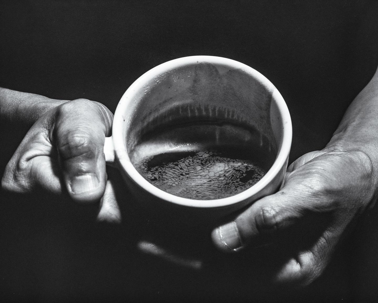 A person's hands hold a mug of coffee, with the surface of the coffee showing a distinct pattern.