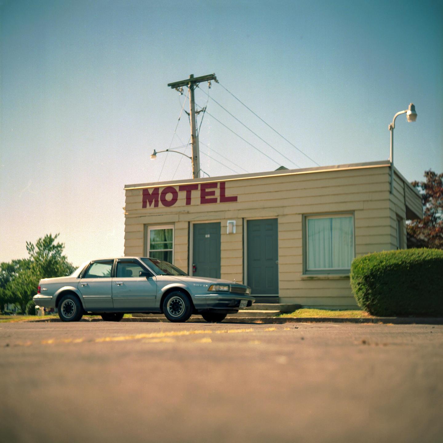 A silver car is parked in front of a motel with a "MOTEL" sign on its facade.