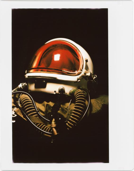 A white high-altitude helmet with a red visor and breathing tubes is shown against a dark background.