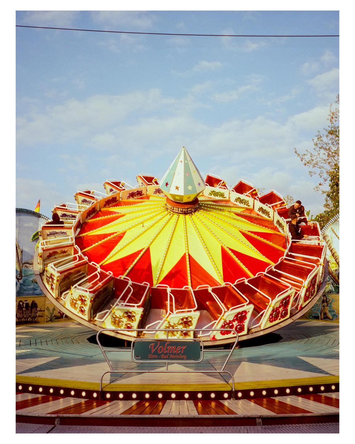 A colorful amusement park ride with red and yellow patterns is captured under a bright blue sky.