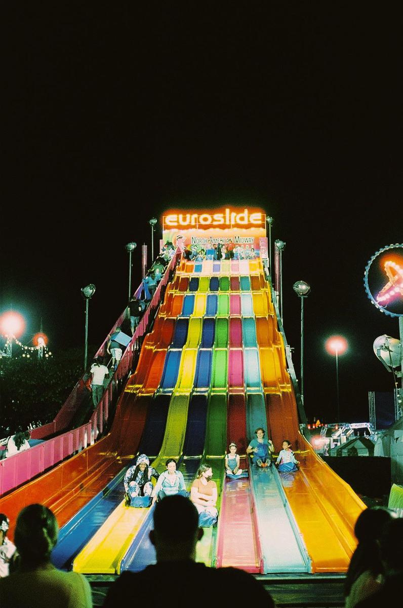 People slide down a colorful amusement park slide at night.