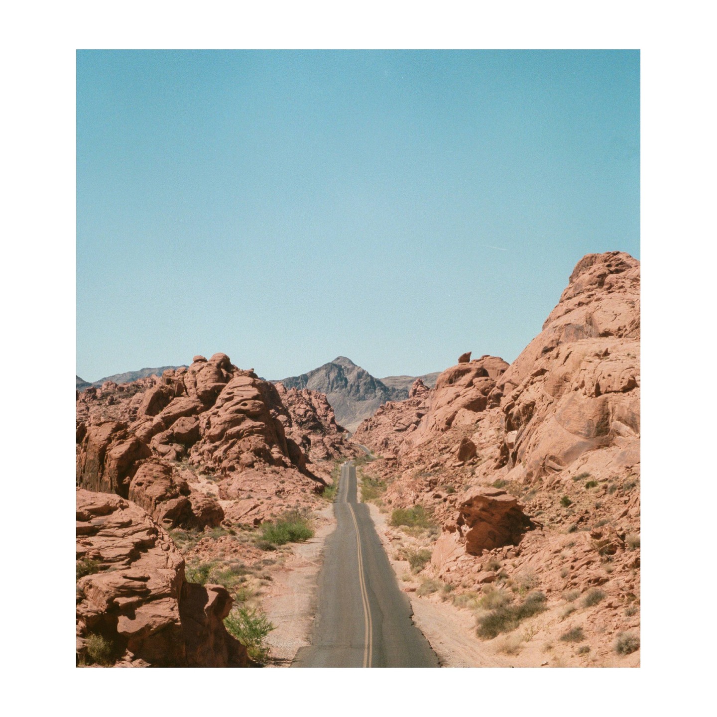 A long road stretches through a valley of red rock formations under a clear sky.