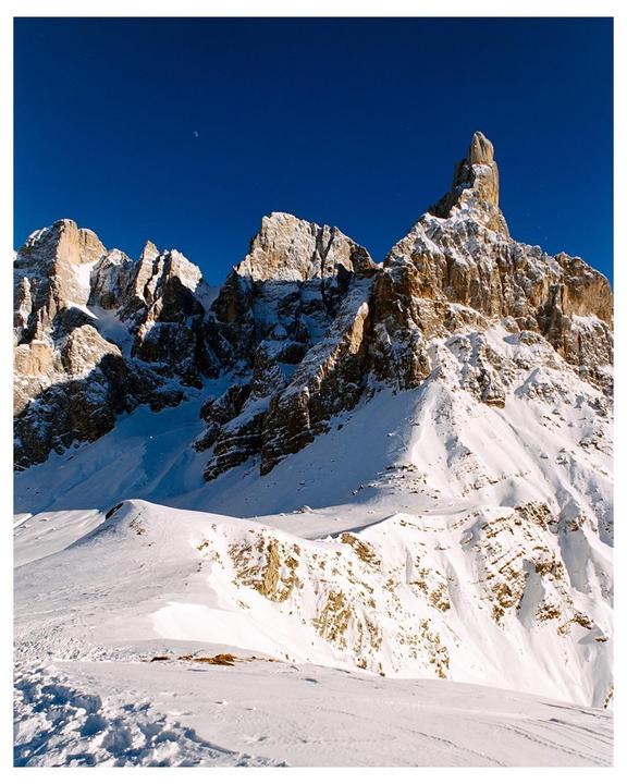 A snow-covered mountain range with a clear blue sky and a crescent moon is visible.