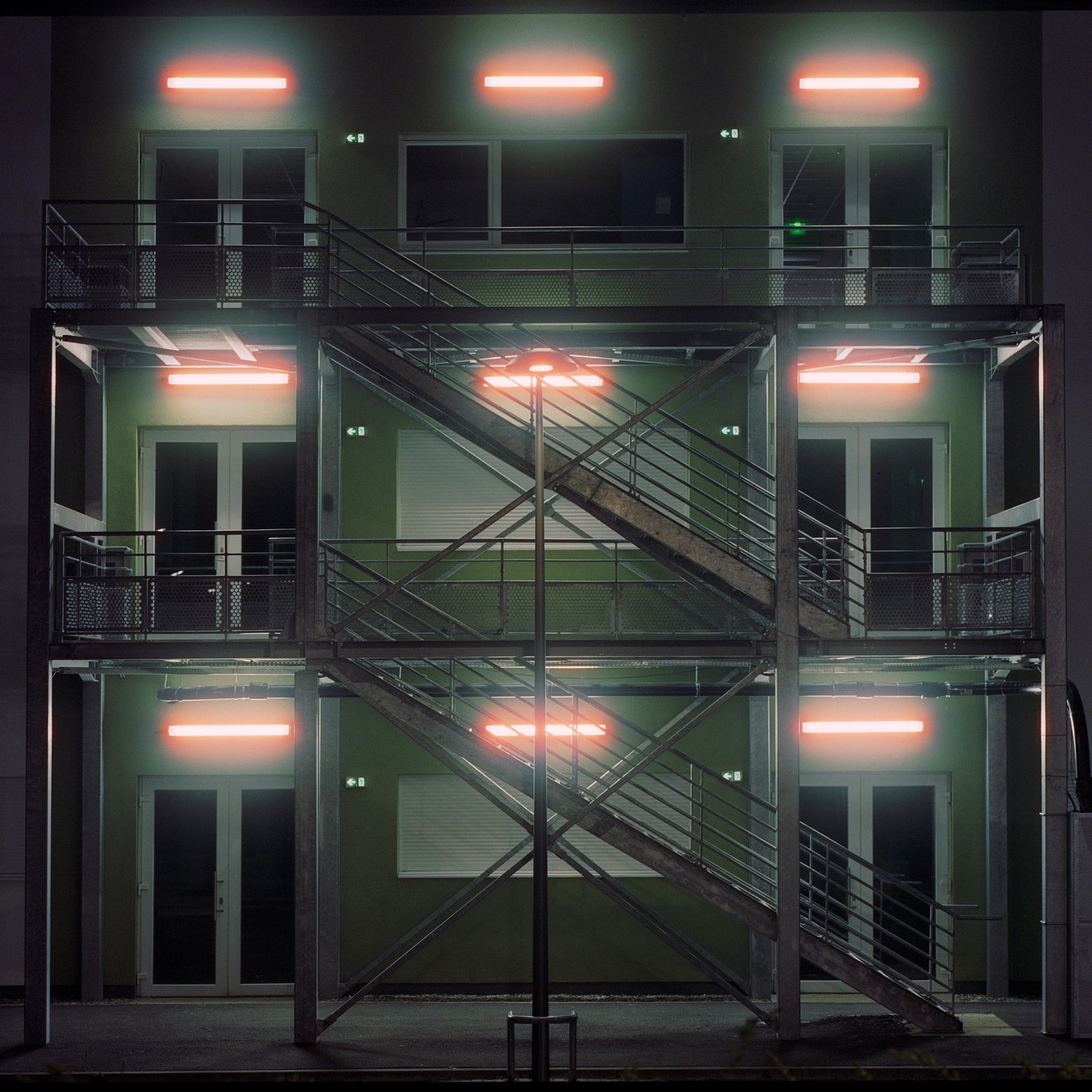 A building with external metal staircases is illuminated by orange neon lights at night.