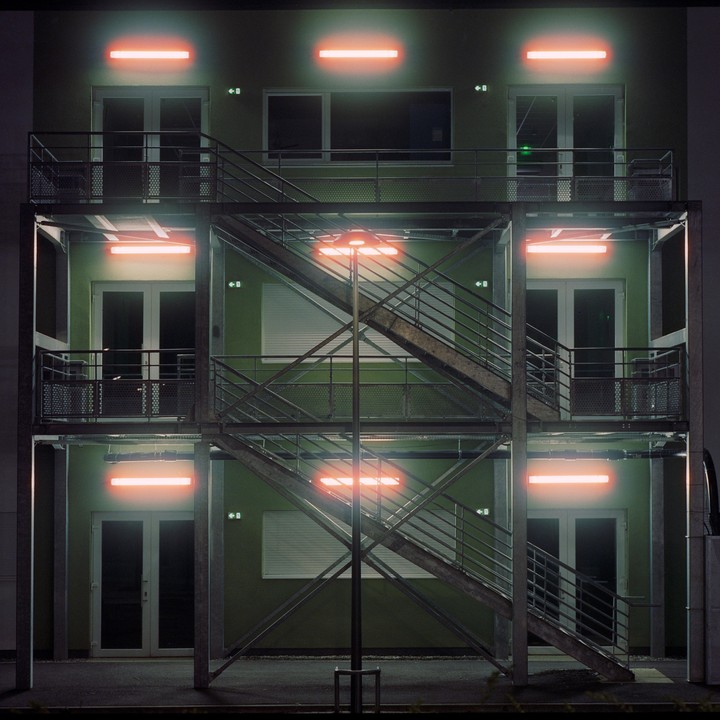 A building with external metal staircases is illuminated by orange neon lights at night.