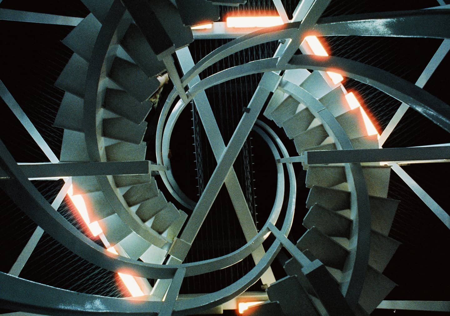 A spiral staircase with orange lights is viewed from above.