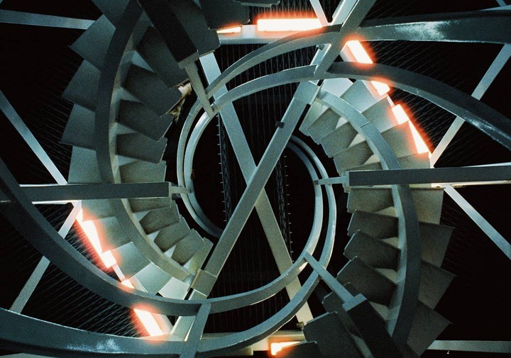 A spiral staircase with orange lights is viewed from above.