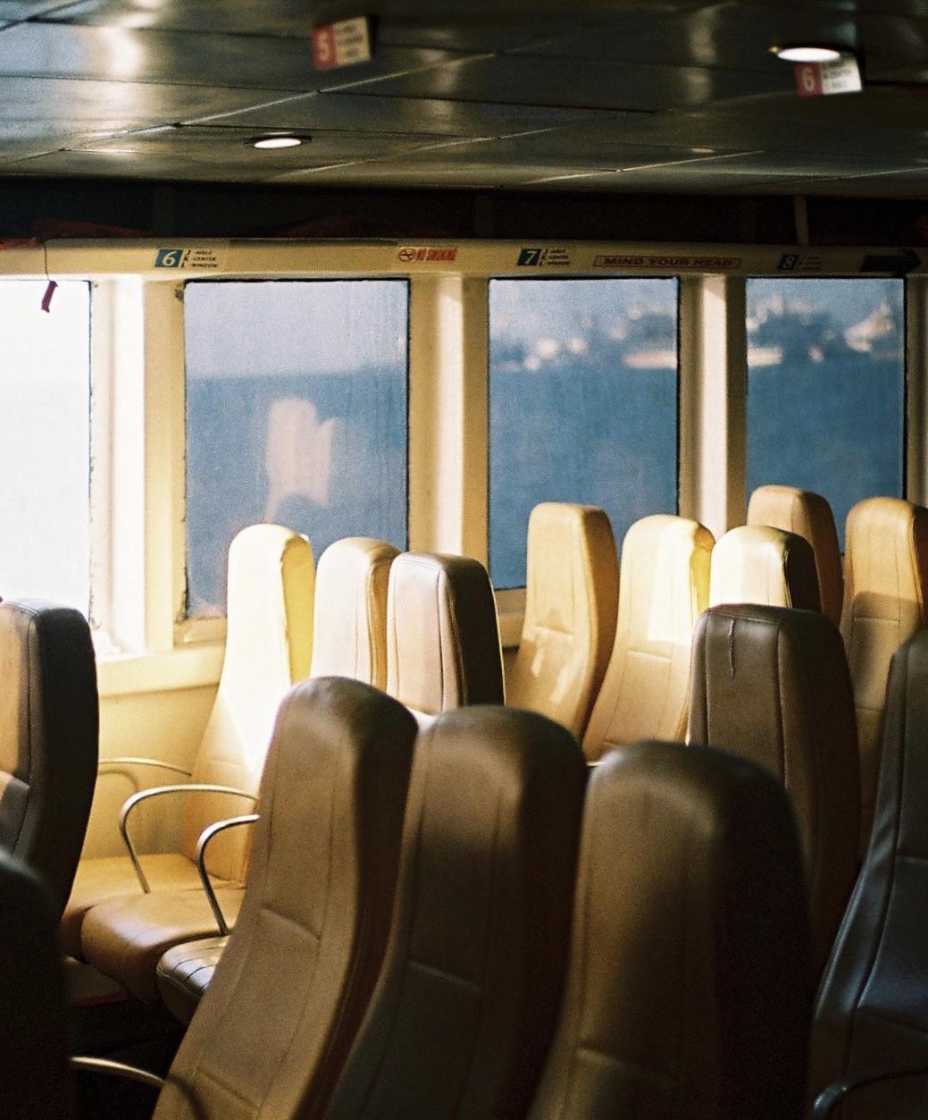 Rows of empty seats face windows looking out onto the water from inside a boat.