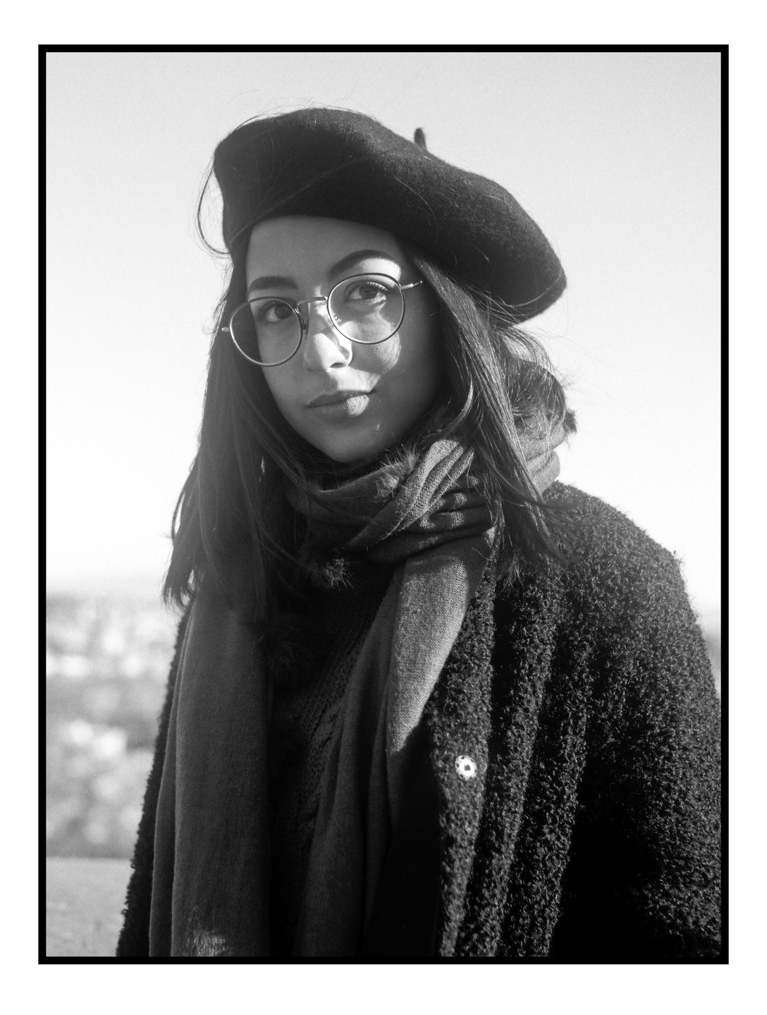 A woman wearing a beret, glasses, and scarf looks directly at the viewer.