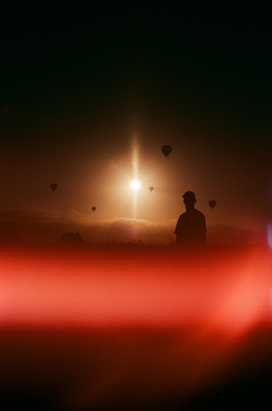 A man watches hot air balloons in the sky during sunset.