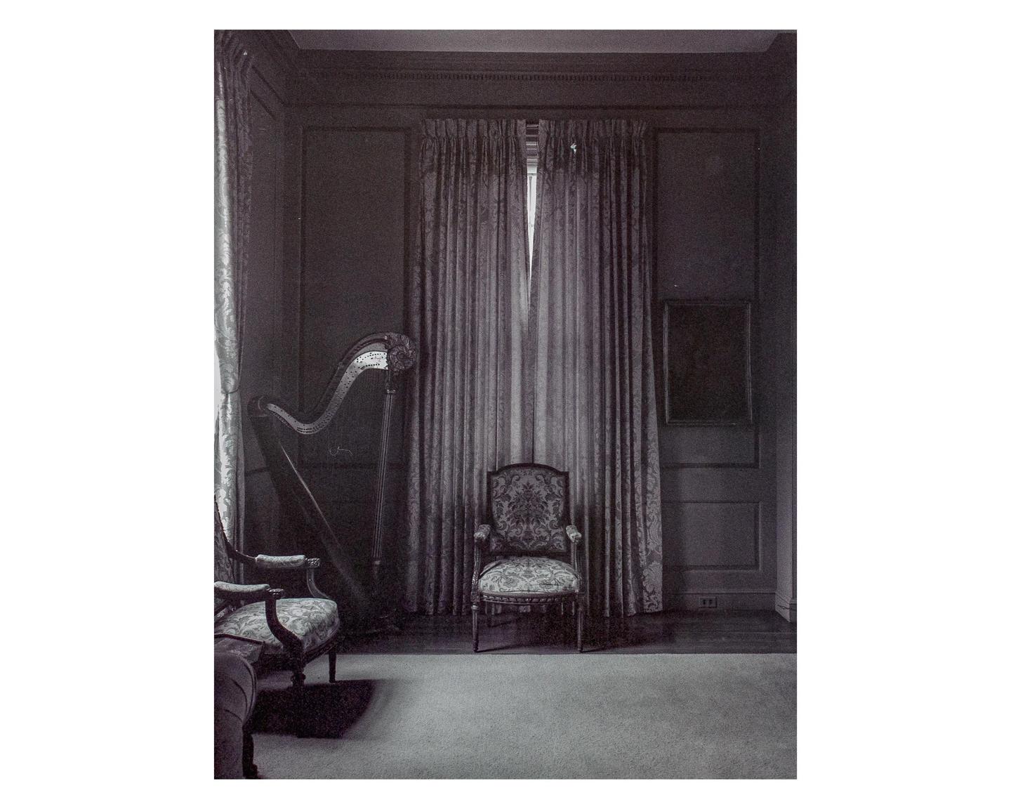 A harp and two ornate chairs are arranged in a dimly lit room with heavy curtains.