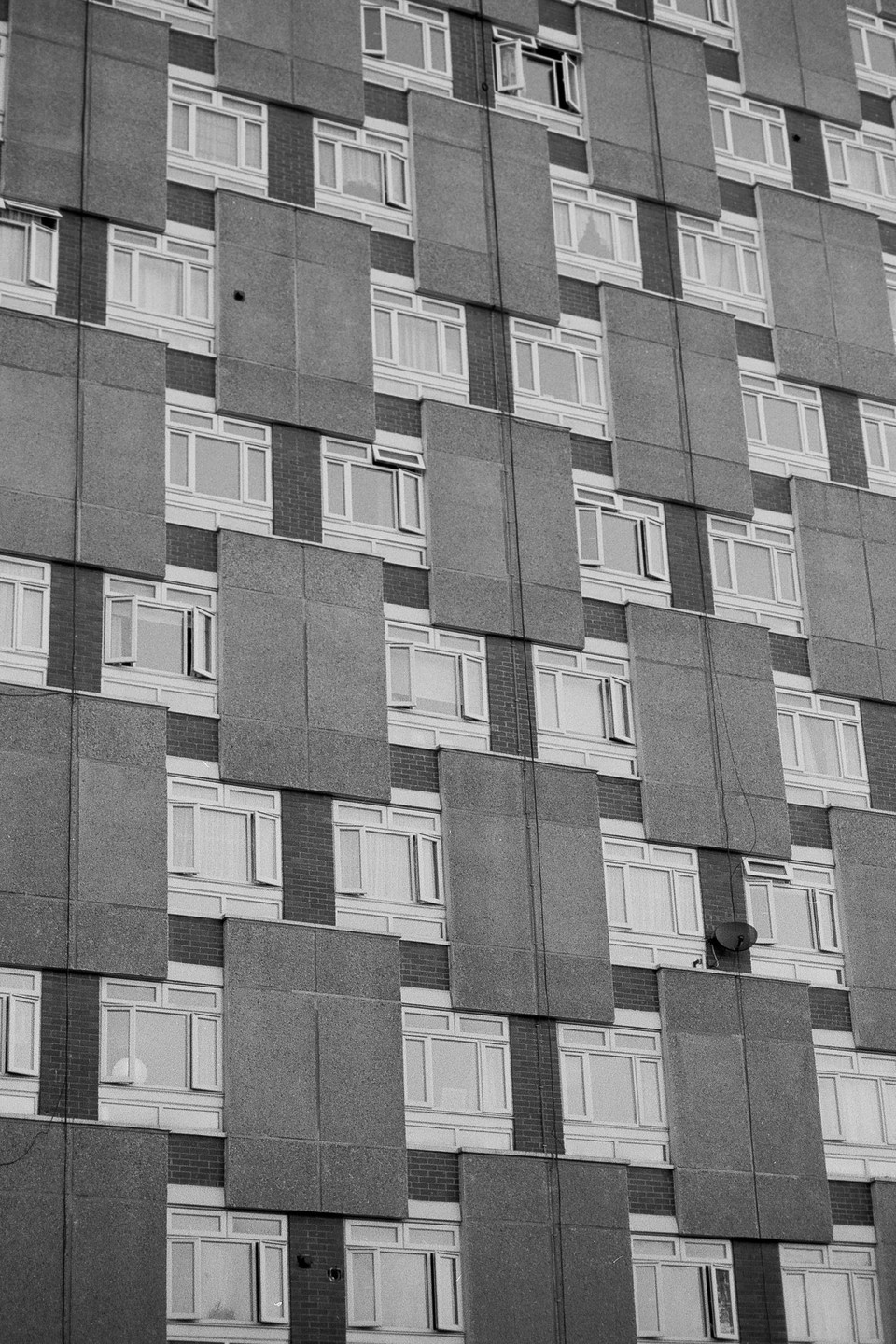 A tall building with a repeating pattern of windows and concrete panels is shown in black and white.
