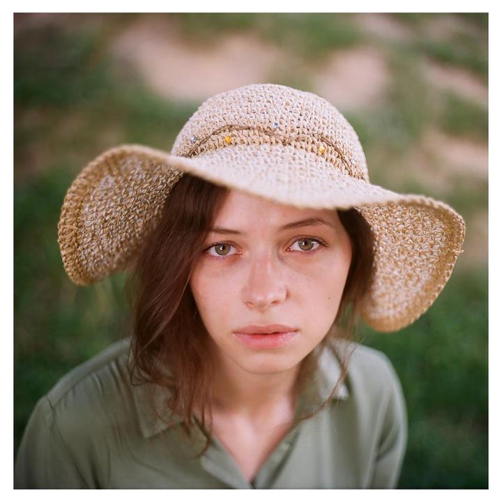 A woman wearing a straw hat looks up at the viewer.