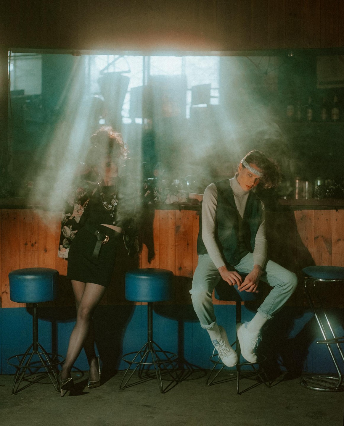 A woman and a man are in a smoky bar with light rays shining through a window.