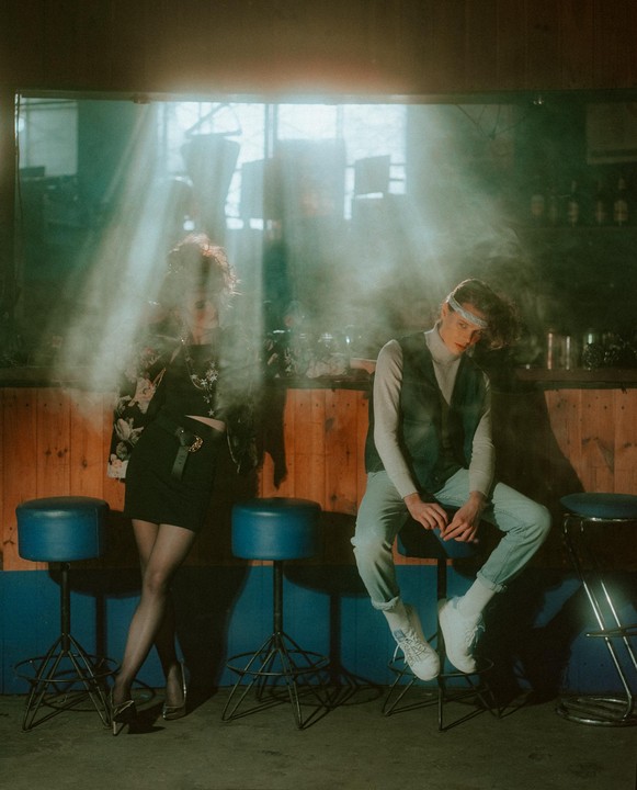 A woman and a man are in a smoky bar with light rays shining through a window.