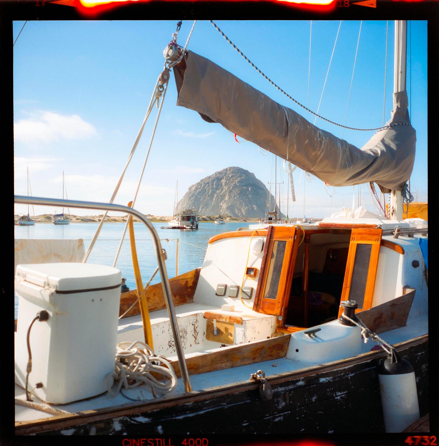 A sailboat is docked in a bay with a large rock formation in the background.