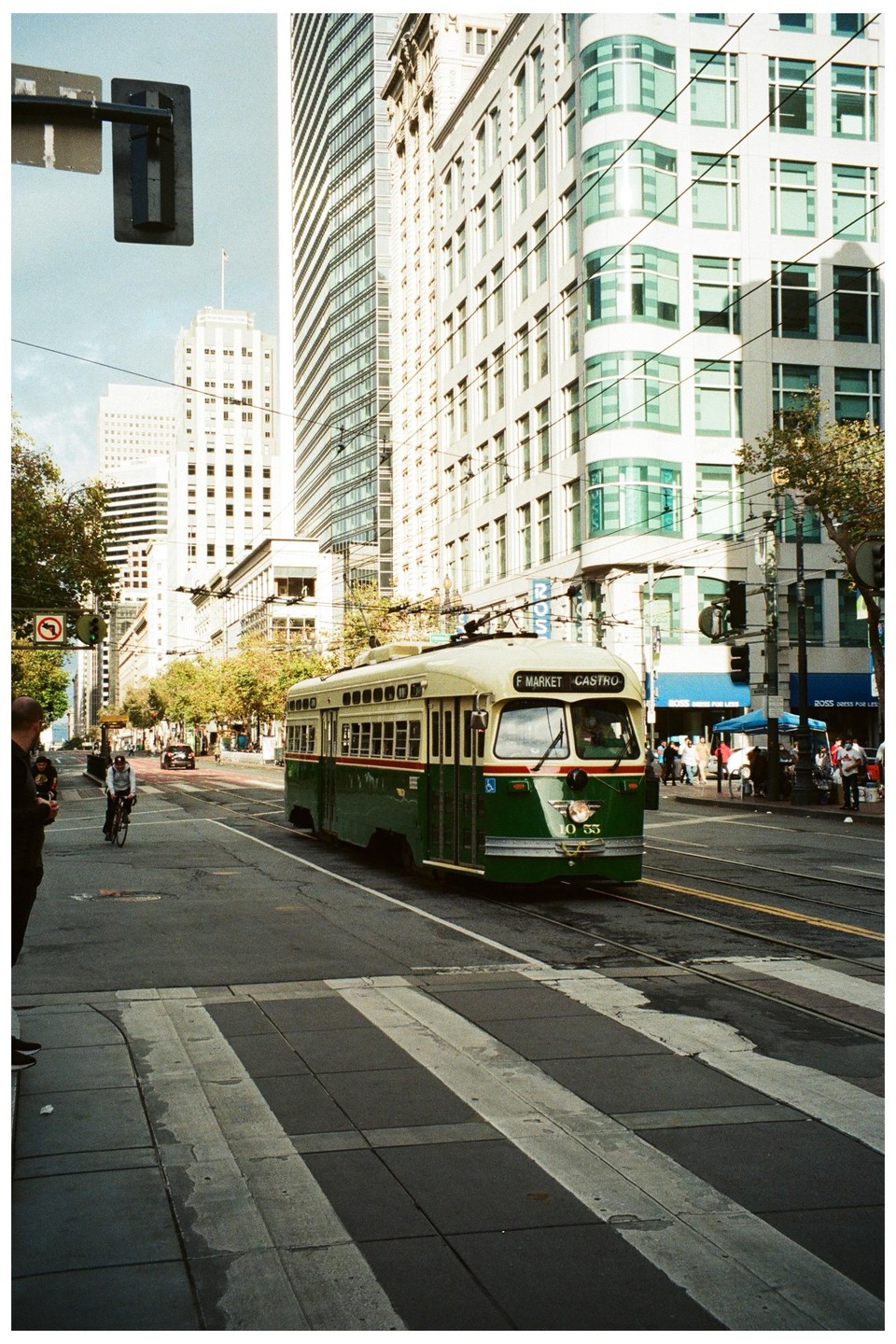 A green and cream streetcar travels down a city street lined with tall buildings.