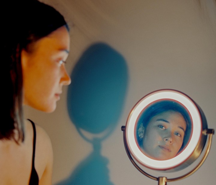 A woman looks at her reflection in a round, illuminated mirror.