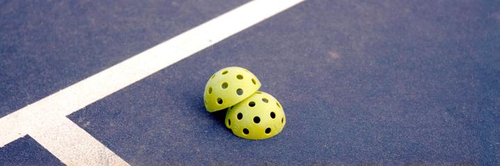 Two yellow pickleball halves are resting on a blue court next to a white line.