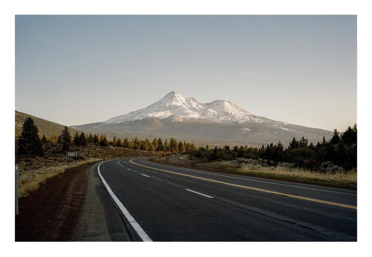 A winding road leads toward a snow-capped mountain under a clear sky.
