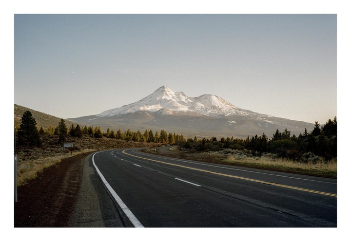 A winding road leads toward a snow-capped mountain under a clear sky.