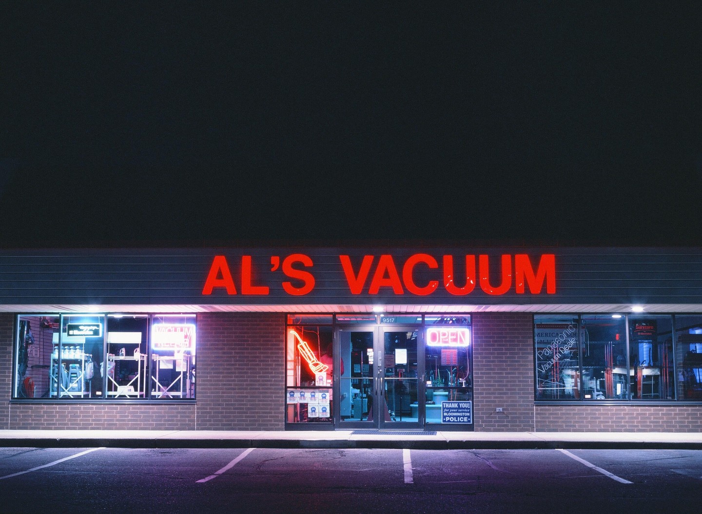 A storefront with a large red neon sign for "AL'S VACUUM" is illuminated at night.