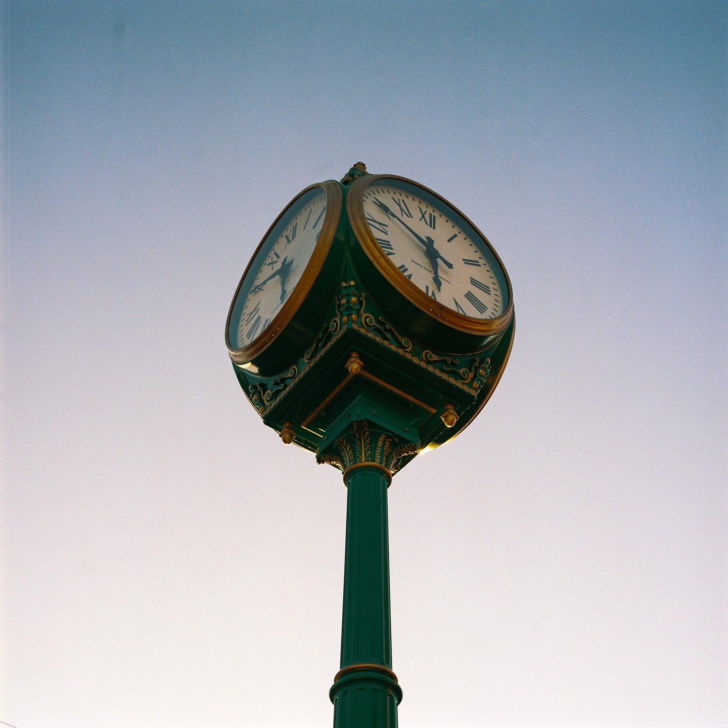 A green street clock with gold accents stands against a clear sky.