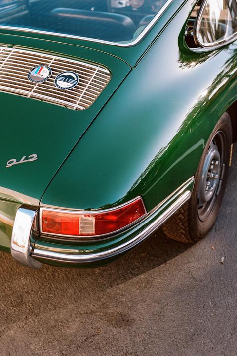 A close-up shot shows the rear of a green vintage car with a chrome bumper and taillight.
