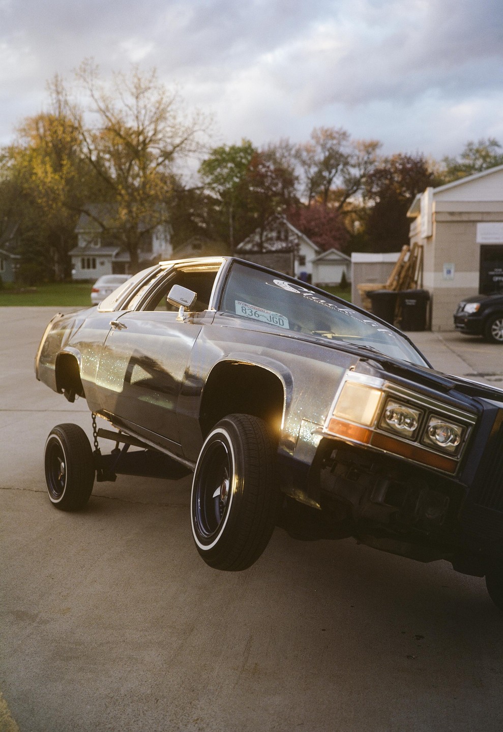 A dark blue lowrider car is shown with its front wheel lifted off the ground.