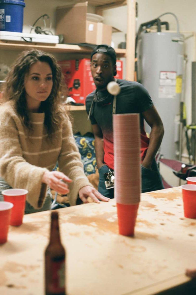 A woman and a man play a game with red cups and a ping pong ball on a wooden table.