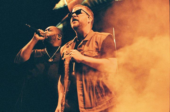 Two men are performing on stage, one singing into a microphone and the other holding a microphone.