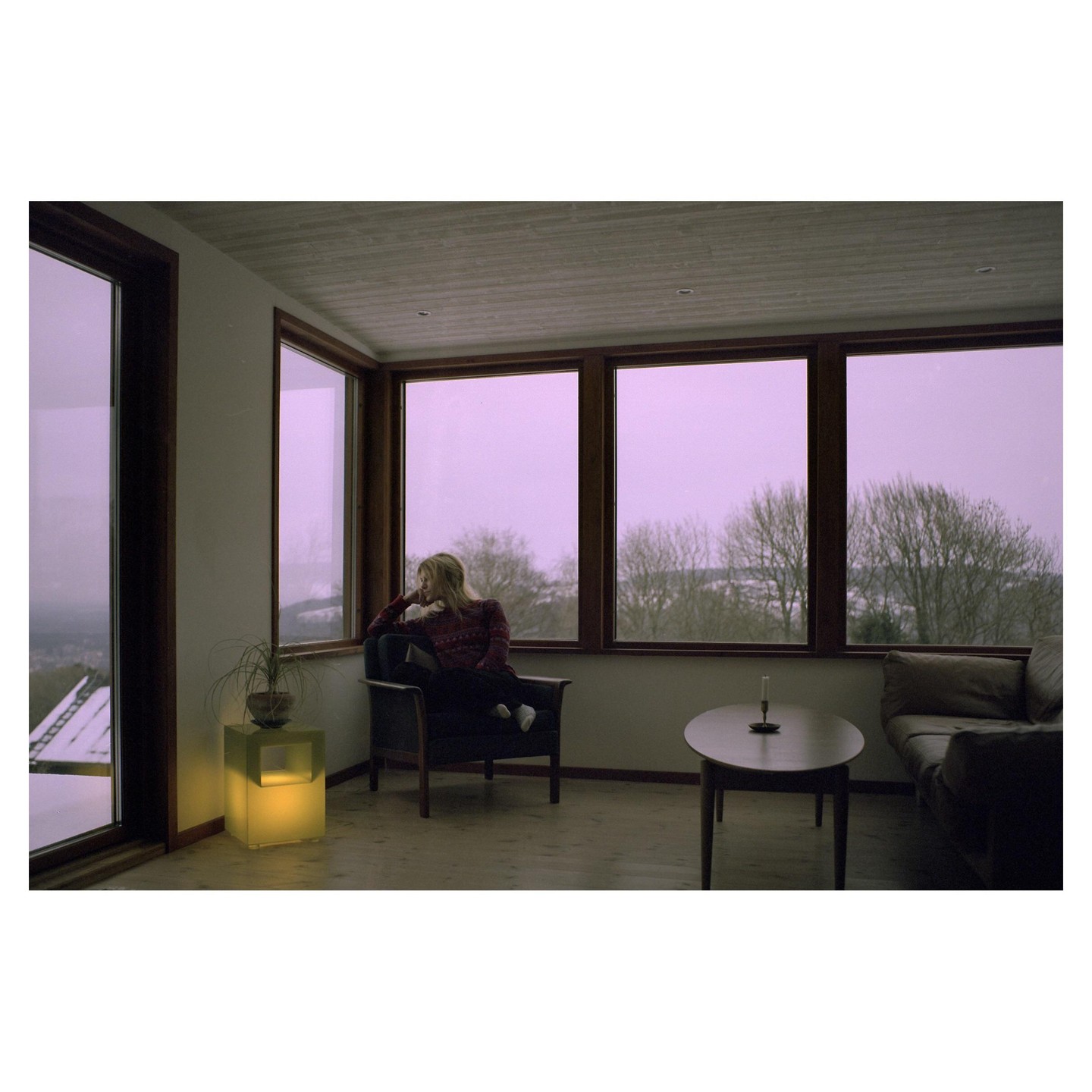 A woman sits in an armchair looking out a large window at a winter landscape.